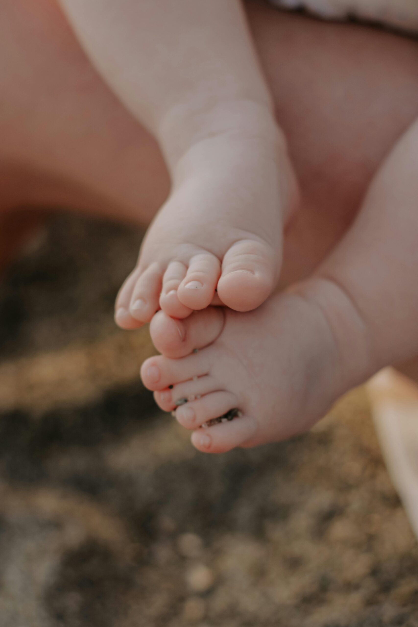 Adorable baby feet with sand, captured closely in soft light on a beach.